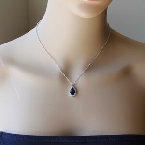 May include: A silver necklace with a teardrop-shaped pendant featuring a dark blue gemstone surrounded by smaller clear gemstones.