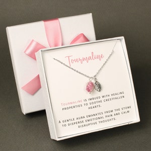 Peut inclure: Une boîte cadeau blanche avec un ruban rose et un collier en argent avec une pierre de tourmaline rose et un pendentif en forme de feuille d'argent. La boîte contient une carte qui dit "La tourmaline est imprégnée de propriétés curatives pour apaiser les cœurs brisés. Une douce aura émane de la pierre pour dissiper la douleur émotionnelle et calmer les pensées perturbatrices."