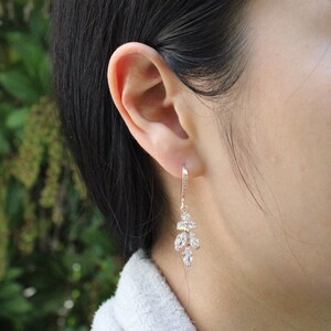 May include: Rose gold dangle earrings with clear cubic zirconia stones. The earrings feature a cluster of stones in a leaf-like design.