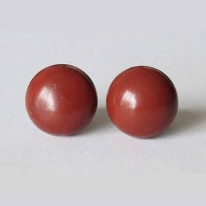 May include: A pair of round, red gemstone earrings. The earrings are smooth and have a glossy finish.