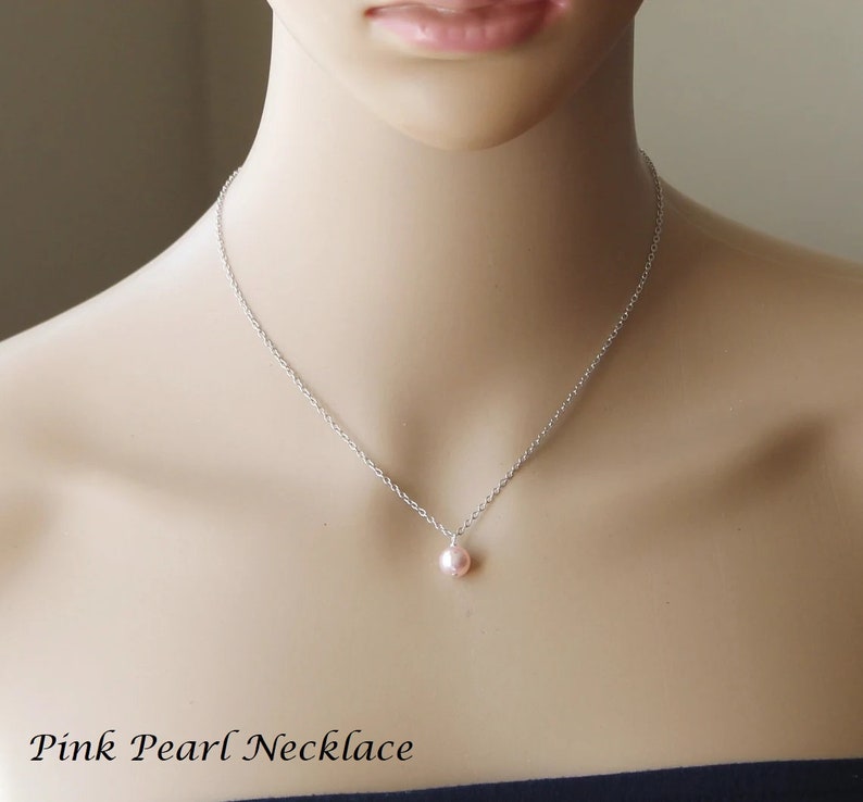 May include: A delicate silver chain necklace with a single pink pearl pendant.  Pink Pearl Necklace.