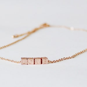 Puede incluir: Un delicado brazalete de cadena dorada con un dije que deletrea "LOVE" en letras may&uacute;sculas.