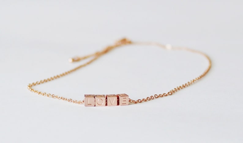 Puede incluir: Un delicado brazalete de cadena dorada con un dije que deletrea "LOVE" en letras may&uacute;sculas.