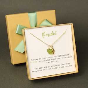 May include: A gold necklace with a green peridot stone and a gold leaf charm. The necklace comes in a small box with a white card that reads "Peridot, known as the "Stone of Compassion", alleviates jealousy, bitterness and greed. The absence of negative emotions promotes positive growth and change."