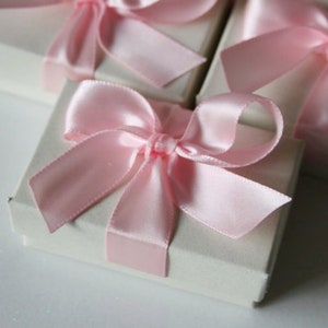 May include: A set of small, white gift boxes with pink satin ribbon bows. The boxes are perfect for small gifts or favors.