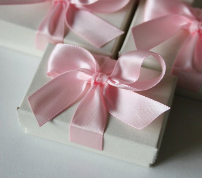 May include: A set of small, white gift boxes with pink satin ribbon bows. The boxes are perfect for small gifts or favors.