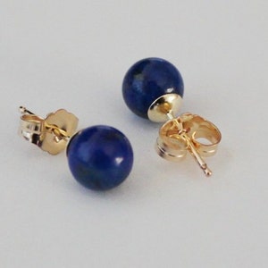 May include: A pair of gold stud earrings with round blue lapis lazuli stones.