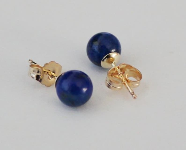 May include: A pair of gold stud earrings with round blue lapis lazuli stones.