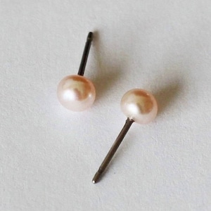 May include: A pair of pearl stud earrings with silver posts. The pearls are a light pink color.