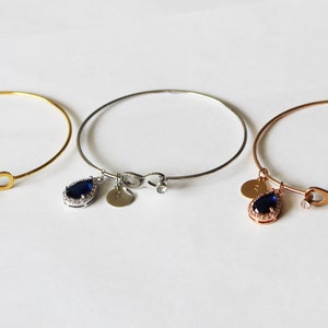 May include: Three delicate bangle bracelets with infinity charm and a teardrop-shaped pendant with a blue gemstone. The bracelets are available in gold, silver, and rose gold.
