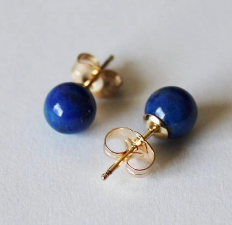 May include: A pair of gold stud earrings with round blue lapis lazuli stones.