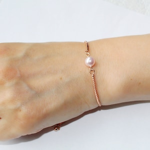 May include: A delicate rose gold bracelet with a single pink pearl charm. The bracelet is adjustable and features a sliding knot closure.