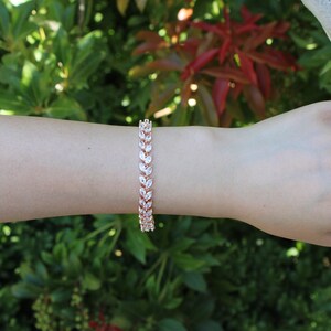 May include: A rose gold bracelet with a leaf design featuring clear cubic zirconia stones.
