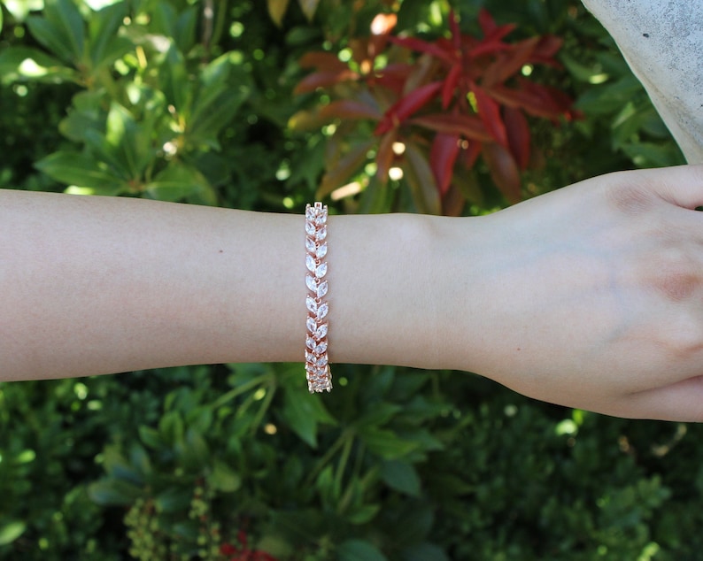 May include: A rose gold bracelet with a leaf design featuring clear cubic zirconia stones.