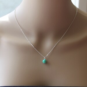 May include: A silver chain necklace with a small, round, green gemstone pendant.