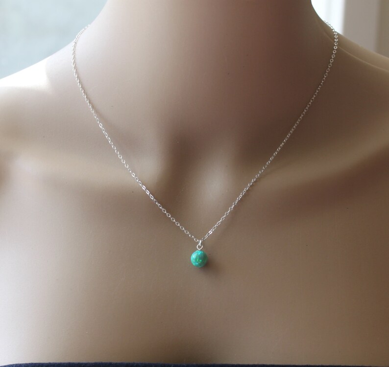 May include: A silver chain necklace with a small, round, green gemstone pendant.