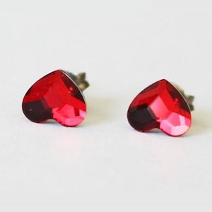May include: A pair of heart-shaped stud earrings with red crystal accents.
