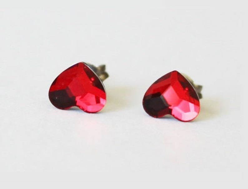 May include: A pair of heart-shaped stud earrings with red crystal accents.