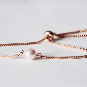 May include: A delicate rose gold chain bracelet with a single pink pearl charm. The bracelet has an adjustable sliding knot closure.
