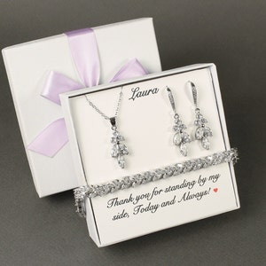 May include: White gift box with a lavender ribbon, containing a silver necklace, earrings, and bracelet with clear crystal stones. The box has a personalized message that reads "Thank you for standing by my side, Today and Always!"