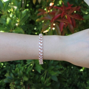 May include: A rose gold bracelet with a delicate leaf design featuring clear cubic zirconia stones.