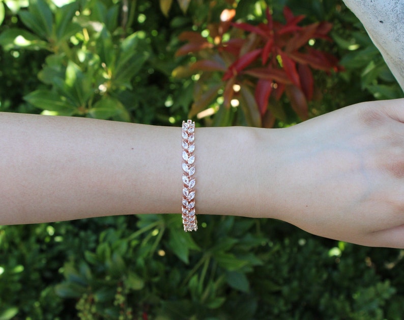 May include: A rose gold bracelet with a delicate leaf design featuring clear cubic zirconia stones.