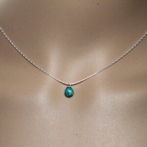 May include: A silver chain necklace with a small, teardrop-shaped blue opal pendant.