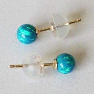 Puede incluir: Un par de pendientes de bot&oacute;n de oro con piedras de &oacute;palo azul. Las piedras tienen un efecto iridiscente brillante.