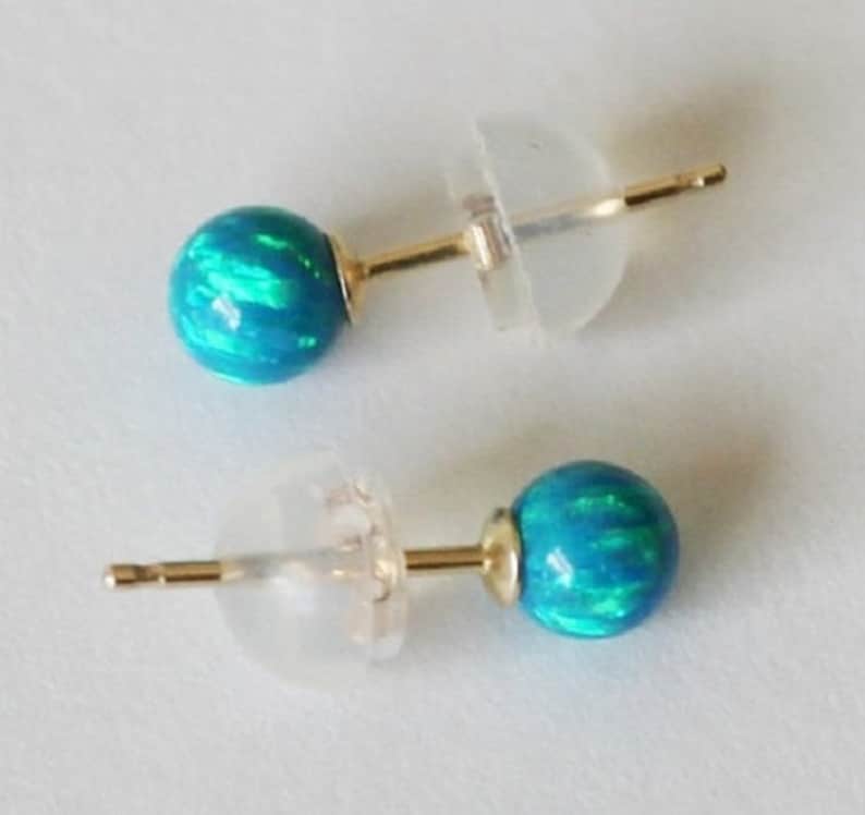 Puede incluir: Un par de pendientes de bot&oacute;n de oro con piedras de &oacute;palo azul. Las piedras tienen un efecto iridiscente brillante.