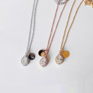 May include: Three delicate necklaces in silver, rose gold, and gold. Each features a teardrop-shaped pendant with a halo of clear stones and a small, round charm with an initial. The chains are fine and the pendants are centered.