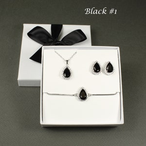 May include: A black teardrop-shaped necklace, bracelet, and earrings set in a white box. The jewelry features a black stone surrounded by clear rhinestones.