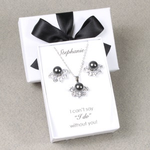 Puede incluir: Una caja de regalo blanca con una cinta negra y un conjunto de collar y pendientes de perlas negras en su interior. La caja tiene una tarjeta blanca con el texto "Stephanie" y "No puedo decir "Sí, quiero" sin ti!"