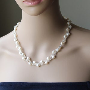 Op de afbeelding: Een witte parelketting met meerdere strengen parels die in elkaar zijn geweven. De ketting is op een wit mannequin.