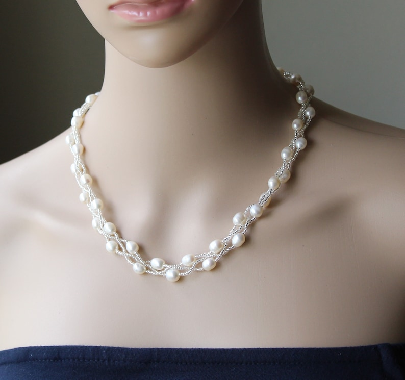 Op de afbeelding: Een witte parelketting met meerdere strengen parels die in elkaar zijn geweven. De ketting is op een wit mannequin.