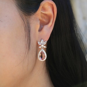 May include: A pair of silver teardrop earrings with a pink crystal center and clear crystal accents.