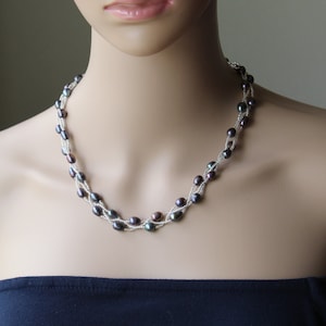 Op de afbeelding: Een meerrijige ketting gemaakt van donkergrijze parels en zilveren kralen. De ketting is gelaagd en gedraaid, wat een uniek en elegant ontwerp cre&euml;ert.