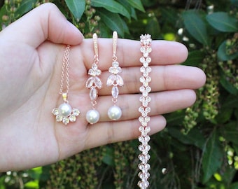 May include: A rose gold jewellery set comprising a necklace, earrings, and bracelet. The necklace features a white pearl pendant surrounded by crystals. The earrings and bracelet are adorned with crystals and white pearls. Text reads "White pearls".