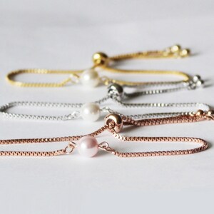May include: Four adjustable pearl bracelets in gold, silver, rose gold, and a pink pearl. Each bracelet has a small pearl charm.