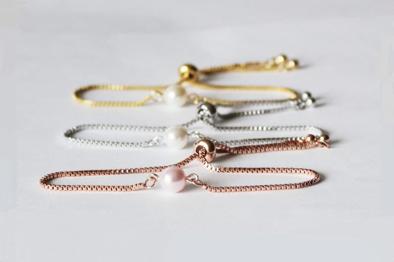 May include: Four adjustable pearl bracelets in gold, silver, rose gold, and a pink pearl. Each bracelet has a small pearl charm.