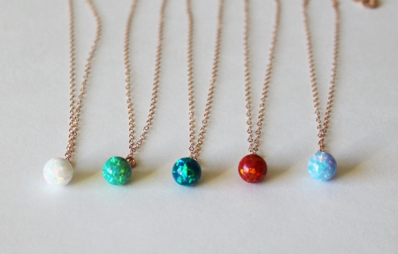 May include: Five delicate necklaces with small opal pendants in various colors, including white, green, blue, and red. The necklaces are made of rose gold chain.