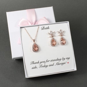 May include: A white gift box with a pink ribbon and a message that reads "Beth Thank you for standing by my side, Today and Always!" The box contains a rose gold necklace and earrings with teardrop-shaped stones.