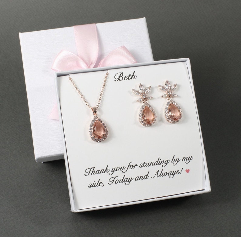 May include: A white gift box with a pink ribbon and a message that reads "Beth Thank you for standing by my side, Today and Always!" The box contains a rose gold necklace and earrings with teardrop-shaped stones.