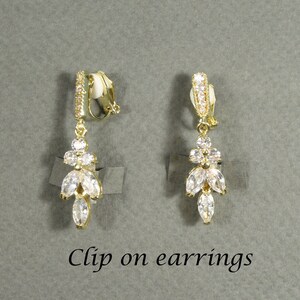 May include: A pair of gold clip-on earrings with a dangling design featuring clear cubic zirconia stones.