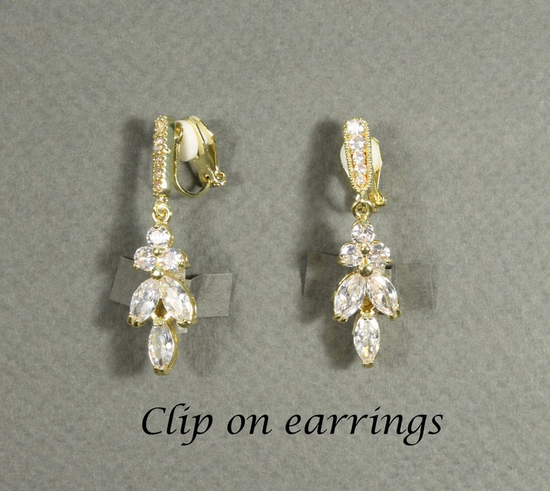 May include: A pair of gold clip-on earrings with a dangling design featuring clear cubic zirconia stones.