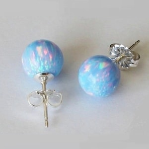 May include: A pair of silver stud earrings with light blue opal round stones. The stones have a pearlescent finish with iridescent pink and green hues.