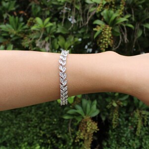May include: A silver bracelet with a delicate, leaf-shaped design. The bracelet is made of small, clear stones that are set in a silver chain.
