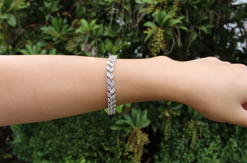 May include: A silver bracelet with a delicate, leaf-shaped design. The bracelet is made of small, clear stones that are set in a silver chain.