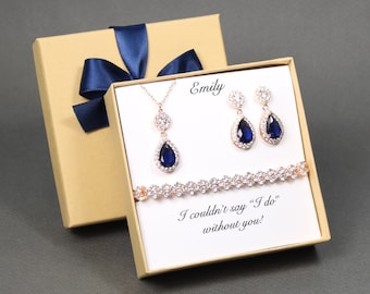 May include: A gift box with a blue ribbon and a card that says "I couldn't say "I do" without you!"  The box contains a rose gold necklace, earrings, and bracelet with blue teardrop-shaped stones.