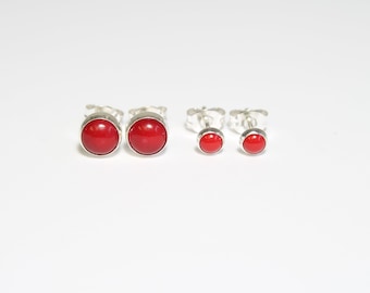 May include: A set of four silver stud earrings with red gemstone accents. The earrings are in two sizes, with the larger pair in the center and the smaller pair on either side.