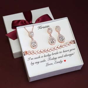 May include: A white gift box with a burgundy ribbon contains a rose gold necklace, earrings, and bracelet with teardrop-shaped crystals. The box has a personalized message that reads "Kristin I'm such a lucky bride to have you by my side, Today and always! Love, Emily"